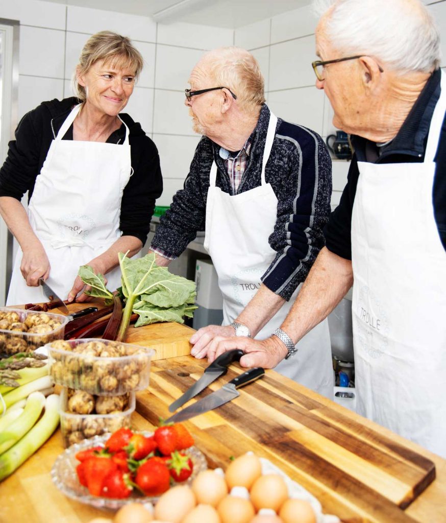 Ældre kvinde og to ældre mænd står i køkkenet og laver mad