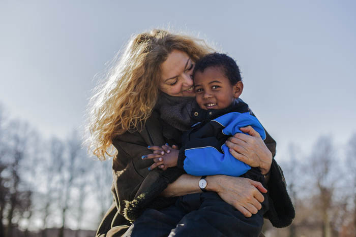 Smilende kvinde omfavner et barn i flyverdragt